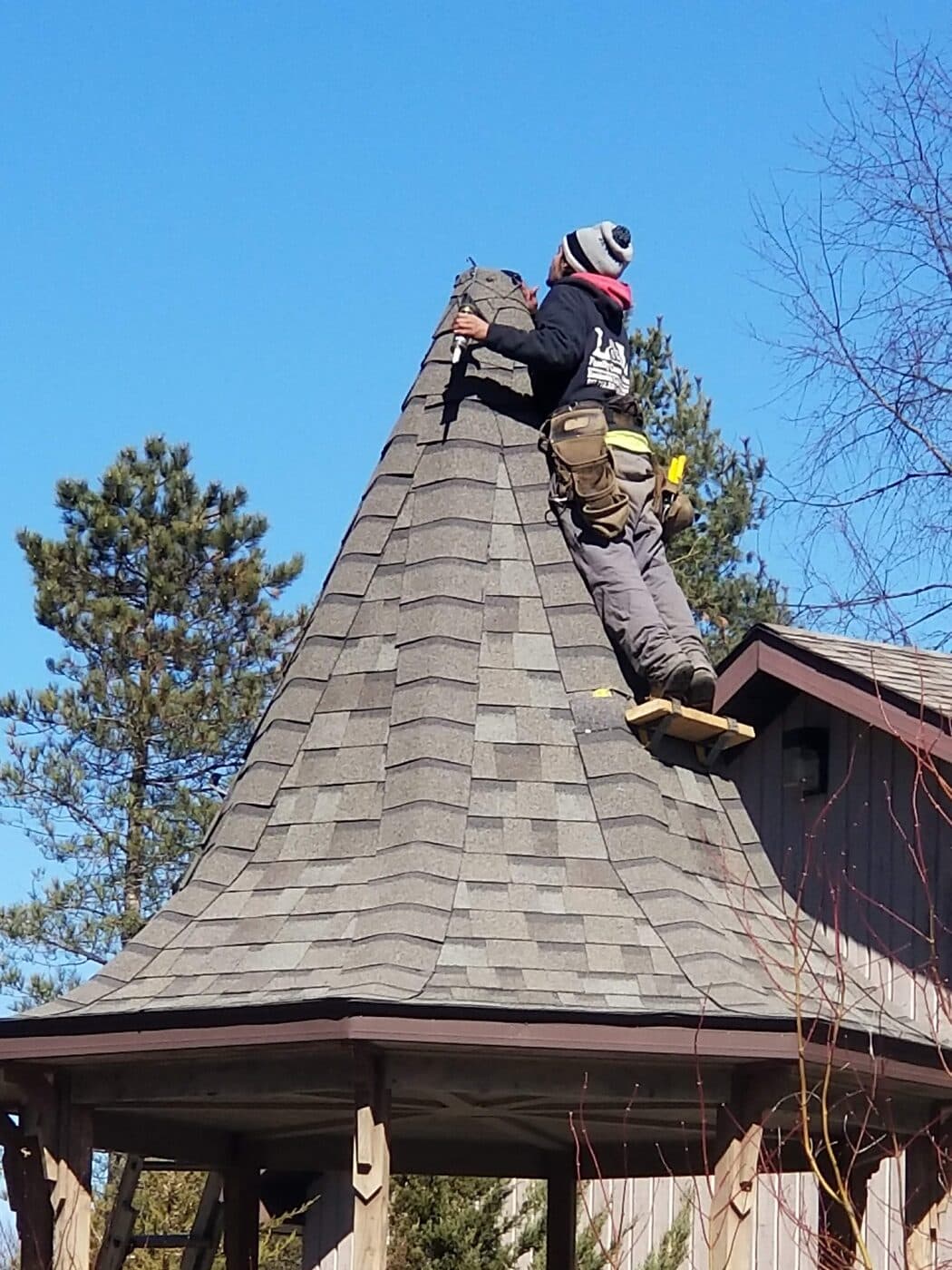Two technicians working at the peak of a gazebo roof against a blue sky