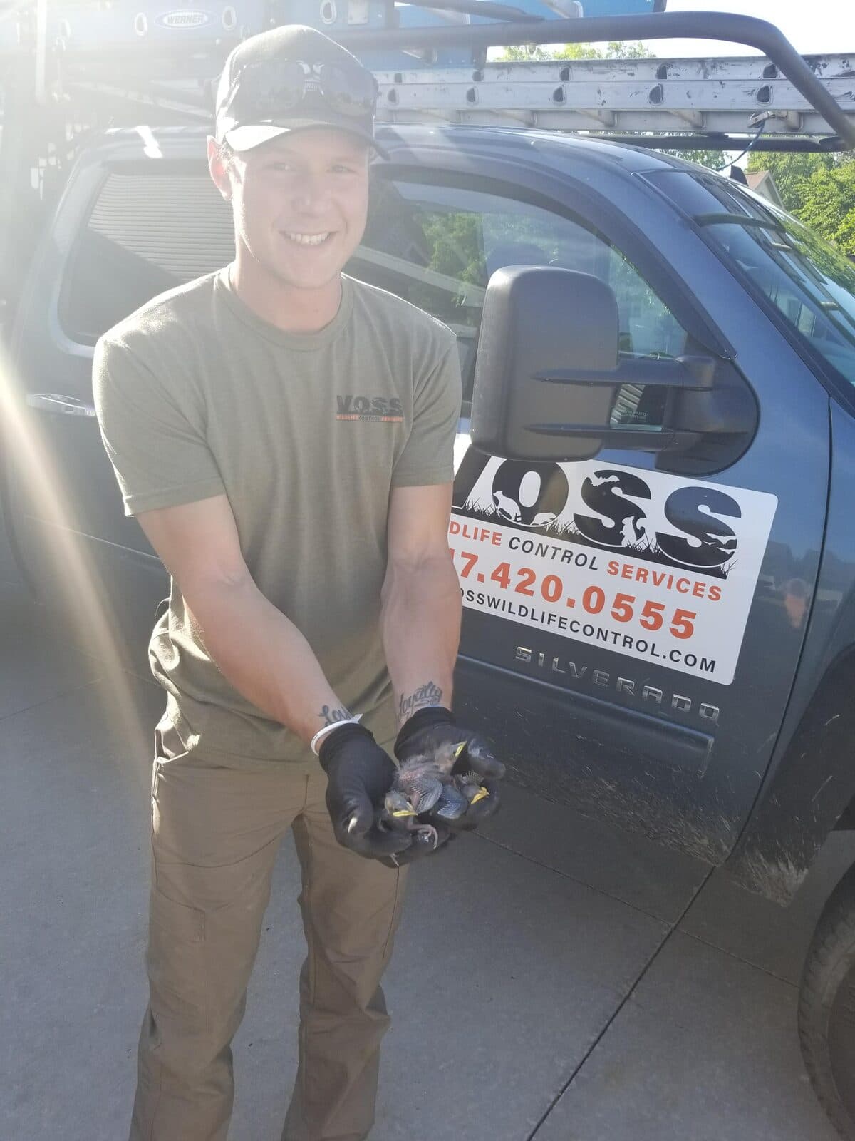A smiling Voss technician holding baby raccoons beside the company truck